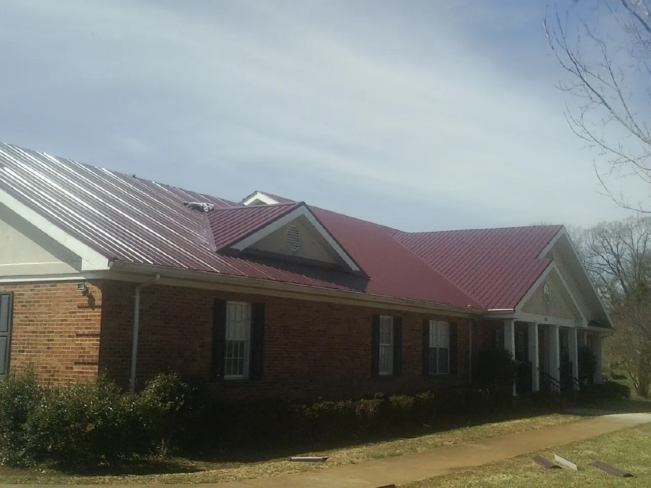 Red metal roof with gabled entries on a long brick building, from a Hail Damage Roof Repair job in Bronson