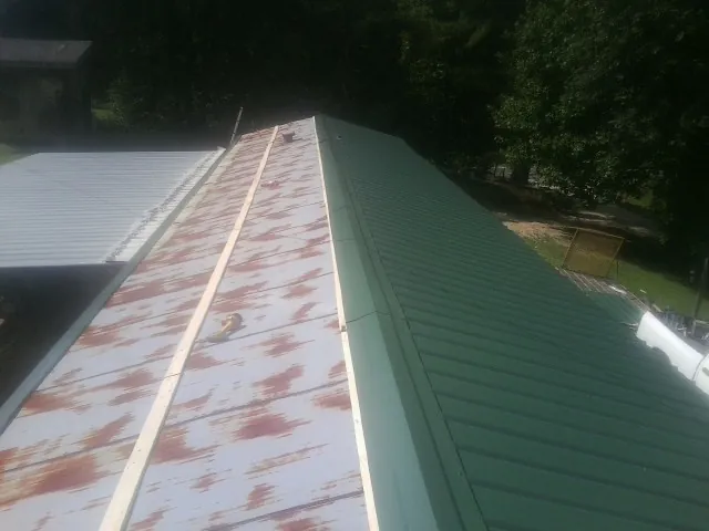 Old rusted panels beside newly installed green metal roofing — Wind Damage Roof Repair by Roofing Brothers in Bronson