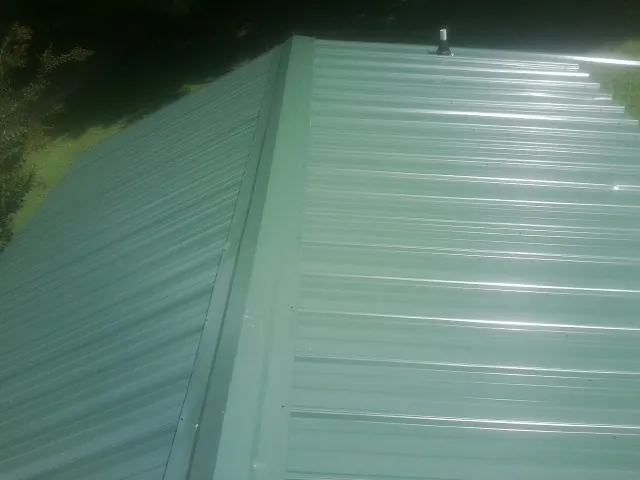 New green metal panels meeting at the ridge of a roof — Flat Roof Repair work by our crew in Bronson