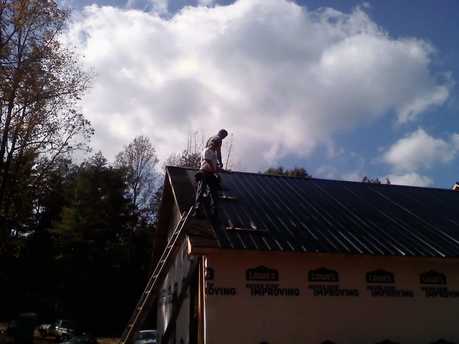 Roofer fastening dark metal panels high against a cloudy sky in Bronson